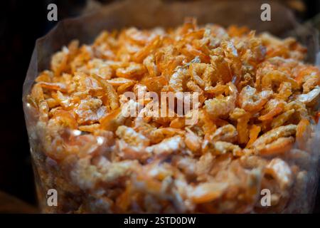 Ein großer Haufen orangener, sonnengetrockneter Garnelen, verpackt in einem transparenten Plastikbeutel, fertig als kulinarische Zutat an einem traditionellen Marktstand. Stockfoto