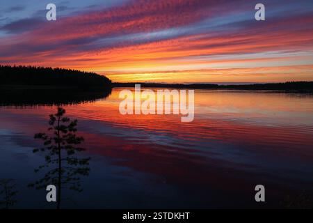 Eine atemberaubende Sommernacht auf dem Kymijoki Fluss. Ein lebhafter Sonnenuntergang färbt den Himmel in Gelb, Rot, Violett und Blau, reflektiert auf dem ruhigen Wasser. Stockfoto