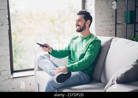 Junger Mann, der bei Tageslicht in einem stilvollen Wohnzimmer Freizeit genießt, lächelnd und entspannt. Stockfoto