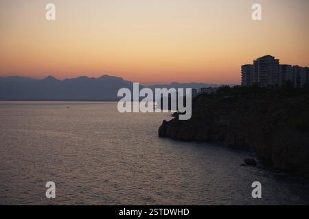 Ein atemberaubender Sonnenuntergang über der Küste von Antalya, mit ruhigem Meer, zerklüfteten Klippen und einer Skyline der Stadt mit entfernten Berglandschaften. Stockfoto