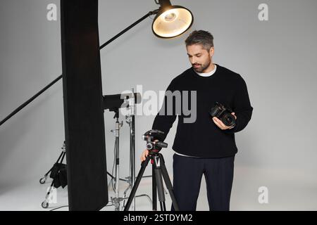 Ein Mann stellt seine Kamera und seine Lichtausrüstung sorgfältig in einem modernen Studio auf, um sich auf ein Foto vorzubereiten. Stockfoto
