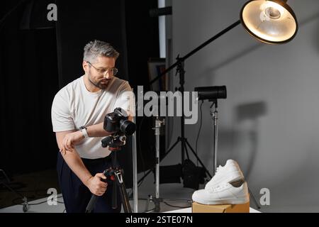 Ein Mann stellt seine Kamera auf, um einen stylischen Sneaker in einem gut beleuchteten Studio aufzunehmen. Stockfoto