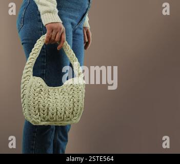 Frau mit beigefarbener Stricktasche vor braunem Hintergrund. Idee des World Strick Day Konzepts. Stockfoto
