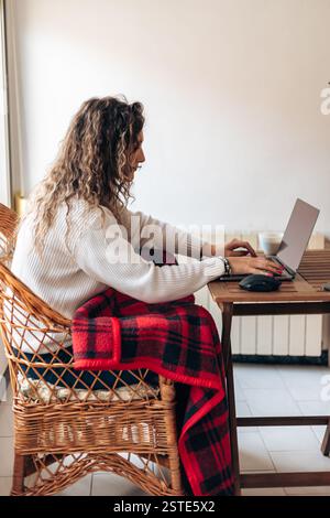 Seitenansicht einer jungen Freiberuflerin, die mit Laptop am Tisch sitzt und Informationen schreibt, während sie an einem neuen Projekt im modernen Zuhause arbeitet Stockfoto