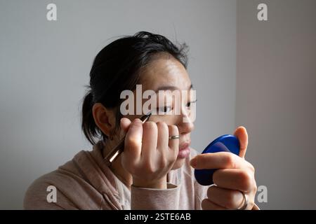 Junge Frau, die zu Hause vor dem Spiegel sorgfältig den Lidstrich aufträgt Stockfoto