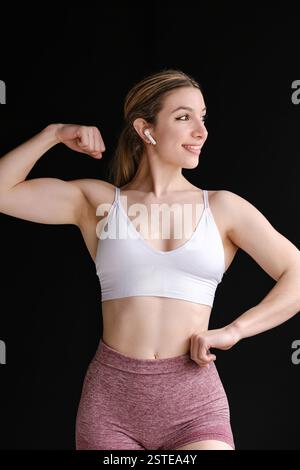 Eine fitte Frau in Activewear steht selbstbewusst vor einem schwarzen Hintergrund und ist auf ihre Trainingsroutine vorbereitet Stockfoto