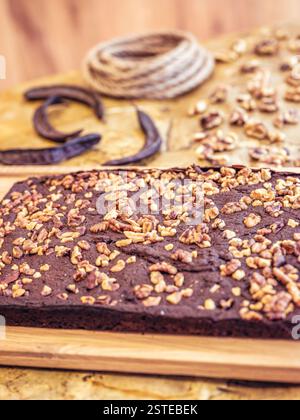 Reichhaltiger Schokoladenkuchen, der großzügig mit knusprigen Walnüssen belegt ist, auf einem rustikalen Holzschneidebrett ausgestellt, mit Hufeisen und Seilen im Stockfoto
