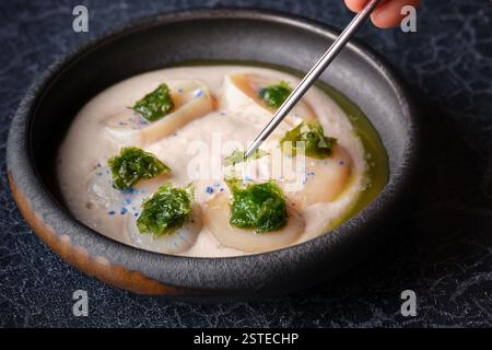 Von oben aus der Ernte, die anonyme Person isst köstliche gekochte Cremesuppe mit Kräutern und Jakobsmuscheln, serviert in einer Schüssel auf dem Tisch Stockfoto