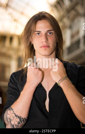 Hübscher, langhaariger junger Mann drinnen in einer eleganten Galerie Stockfoto