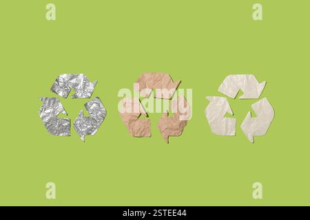 Drei Recyclingsymbole aus Aluminiumfolie, braunem Papier und Kunststoff vor einem grünen Hintergrund, die nachhaltige Praktiken und Öko-fri symbolisieren Stockfoto