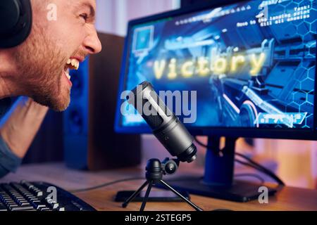 Schreiend und feiert den Sieg. Online-Streamer, der FPS-Shooter zu Hause spielt. Stockfoto