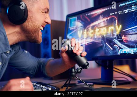Schreiend und feiert den Sieg. Online-Streamer, der FPS-Shooter zu Hause spielt. Stockfoto