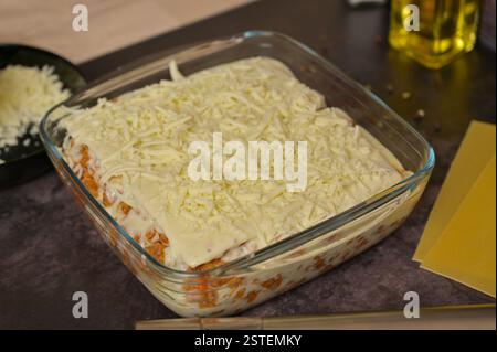 Hausgemachte Lasagne-Zubereitung. Geriebener Käse, Bolognese-Sauce in Glasform. Lasagne Nudelblätter. Käse in einer schwarzen Schüssel. Schwarzer Hintergrund Stockfoto