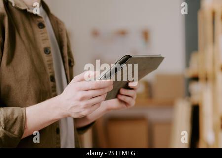 Person, die ein digitales Tablet verwendet, während sie in einem modernen Büro steht und sich auf arbeitsbezogene Aufgaben konzentriert, mit Regalen im Hintergrund Stockfoto