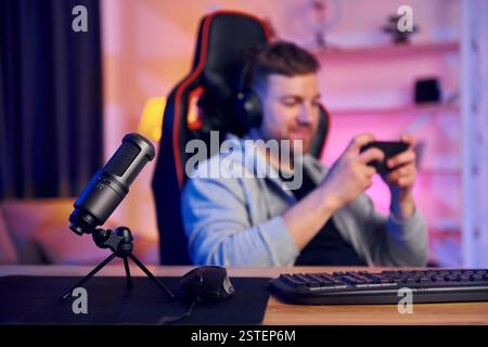 Mit Smartphone in der Hand. Mann mit Kopfhörer und Mikrofon ist live im Stream. Stockfoto