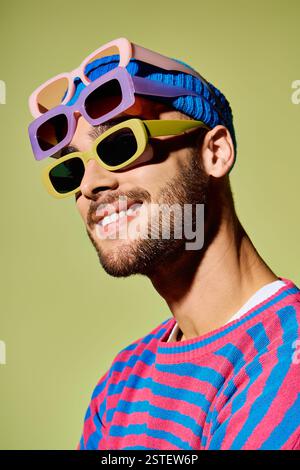 Dieser stilvolle junge Mann zeigt seine trendige Sonnenbrille in einem farbenfrohen Studio. Stockfoto