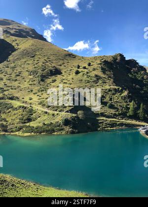 Ein atemberaubender türkisfarbener See reflektiert den klaren blauen Himmel, umgeben von sanften grünen Hügeln Stockfoto