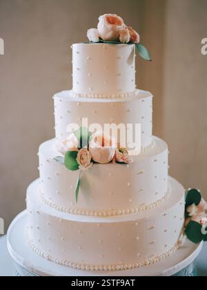 Eine atemberaubende dreistöckige Hochzeitstorte mit glattem weißem Zuckerguss und floralen Akzenten für jede Feier. Stockfoto
