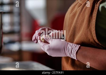 Zugeschnittener Schuss von nicht erkennbarer schwarzer Bäckerin, die in Nitril-Einweghandschuhen arbeitet und ein Stück rohen Teigs bildet, der runde Weizenkörtchen in der Backstubenküche herstellt, Kopierraum Stockfoto