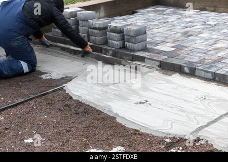 Der Arbeiter installiert Pflastersteine für einen Weg im Freien, um eine stabile und ansprechende Oberfläche zu gewährleisten. Praktische Anwendung der Konstruktionstechniken visibl Stockfoto