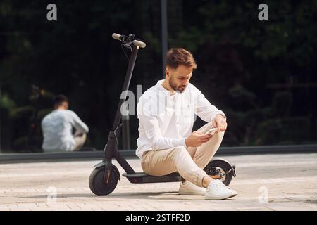 Auf dem Roller sitzen. Stilvoller Mann ist tagsüber draußen. Stockfoto