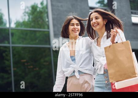 Lächelnd und redend. Zwei Freundinnen haben einen Einkaufstag. Gehen Sie draußen mit Taschen. Stockfoto