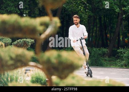 Wunderschöne Bäume und Natur. Ein stilvoller Mann ist tagsüber mit seinem Roller im Freien. Stockfoto
