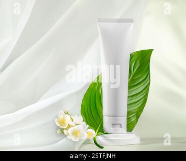 Die leere Tube für weiße Hautpflegeprodukte ist von leuchtend grünen Blättern und zarten weißen Blüten umgeben Stockfoto