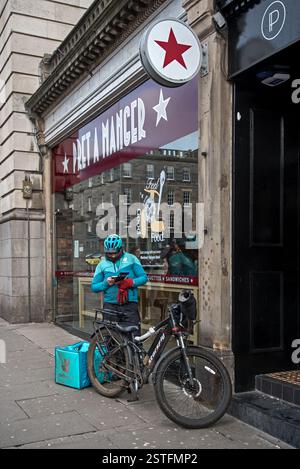 Deliveroo Essenskurier überprüft sein Handy vor einem Pret a Manger in Edinburgh, Schottland, Großbritannien. Stockfoto