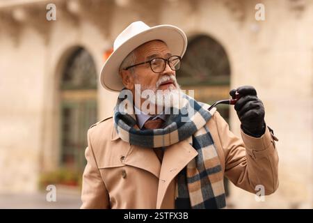 Stilvoller Seniorenmann mit Tabakpfeife auf der Stadtstraße Stockfoto