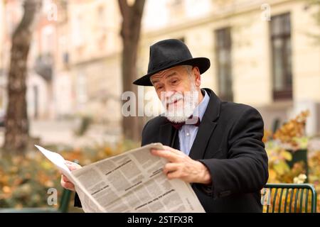 Eleganter bärtiger Mann, der auf der Bank im Park Zeitung liest Stockfoto