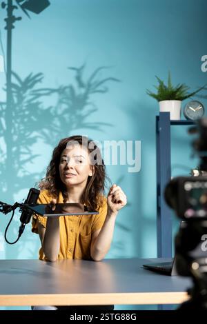 Ein optimierter Techniker präsentiert ein Tablet in der Einstiegsklasse für niedrige Budgets, das aus dem schwach beleuchteten Heimstudio filmt. Jolly Tech Content Creator prüft digitale Geräte vor Online-Publikum Stockfoto
