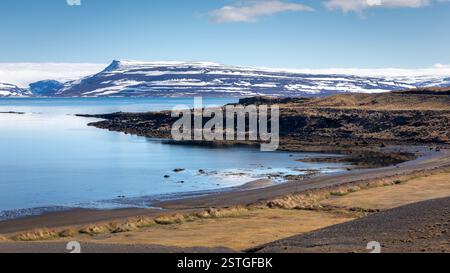 Westjorde Küstenlandschaft in Island mit kristallklarem Wasser, schneebedeckten Bergen und blauem Himmel. Stockfoto