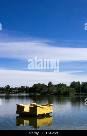 Eine schwebende gelbe rechteckige Skulptur, die auf einem See im Botanischen Garten von Denver schwimmt, mit dramatischem Kontrastlicht und klarem blauem Himmel Stockfoto