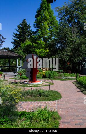 Eine auffällige rote Calder-Kopf- und Gesichtsskulptur steht im Kontrast zum umliegenden Grün des botanischen Gartens in Denver, Colorado. Stockfoto