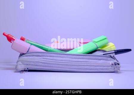 Graue Bleistiftetui gefüllt mit einer Mischung aus farbigen Textmarkern und einem schwarzen biro Stift auf weißer Oberfläche und Hintergrund. Stockfoto