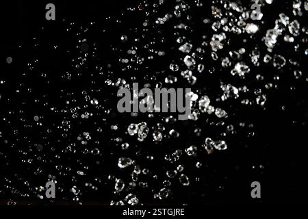 Schwebender Wasserhintergrund. Wassertropfen fliegen in der Luft mit unscharfen Lichtern im Hintergrund Stockfoto