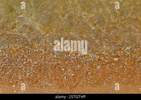 Welle Transparent Meerwasser über Sandstrand mit kleinen Kieselsteinen Hintergrund Stockfoto