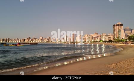 Wenn die Sonne untergeht, spiegeln sich die goldenen Lichter der Stadt wunderschön auf dem ruhigen Meereswasser und erzeugen ein faszinierendes Leuchten entlang der Küste. Stockfoto