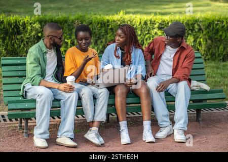 Begeisterte afroamerikanische Freunde diskutieren über Startup- und Online-Arbeit während der Pause im Park Stockfoto