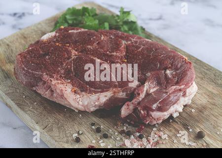 Rohes Schweinesteak, Schweinehals, auf einem Schneidebrett, Marmortisch, Blick von oben, mit Gewürzen und Koriander, keine Leute Stockfoto