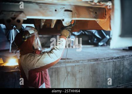 Ein Mechaniker, der Schutzkleidung trägt, inspiziert die Unterseite eines Fahrzeugs in einer Garage Stockfoto
