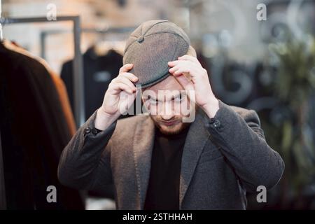Ein Mann in einem Bekleidungsgeschäft passt seinen stylischen Hut an und präsentiert moderne Mode Stockfoto