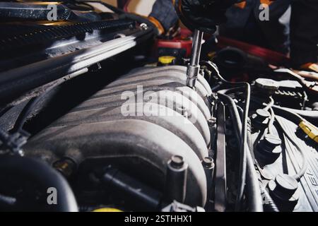 Mechaniker, der einen Schraubenschlüssel an einem Fahrzeugmotor verwendet, schwarze Handschuhe trägt und Wartungsarbeiten hervorhebt Stockfoto