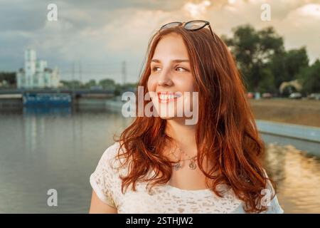 Porträt einer lächelnden jungen rothaarigen Frau über der Flusslandschaft der Stadt Stockfoto