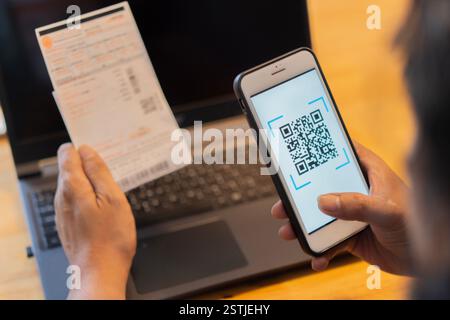 Männliche Hand, die ein Mobiltelefon hält, um den QR-Code für die Rechnung über die App zu scannen. Online-Bezahlung von zu Hause aus. Stockfoto