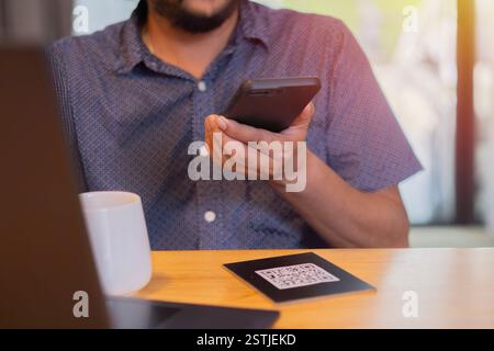 Mann scannt mit dem Smartphone QR-Code für Menü auswählen und Menü bestellen im Café-Restaurant mit digitaler Lieferung. Selektiver Fokus. Stockfoto