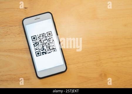Barcode-Leser, QR-Code-Zahlung, bargeldlose Technologie, Digital Money Concept. QR-Code auf dem mobilen Bildschirm über hölzernem Hintergrund mit Kopierraum. Stockfoto