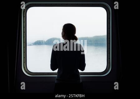 Silhouette einer Frau, die vor dem Fenster in der Fähre steht Stockfoto