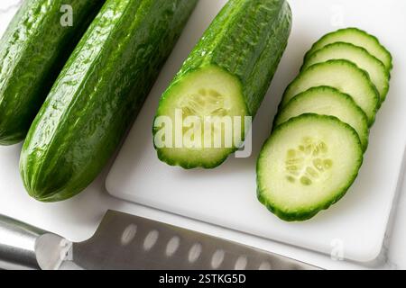 Saftige Scheiben und halbe Gurke auf einem weißen Schneidebrett. Kalorienarmer Snack von rohem Gemüse. Vegetarischer Salat, Bio-Gemüse, Erntekonzept. Stockfoto